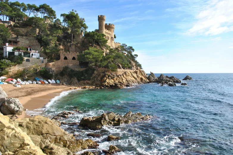 a castle sitting on top of a cliff next to the ocean, in barcelona, lush surroundings, on beach, spikey rocks