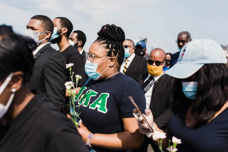 a group of people wearing face masks and holding flowers, by Winona Nelson, unsplash, nipsey hussle, funeral, sea - green and white clothes, skies behind