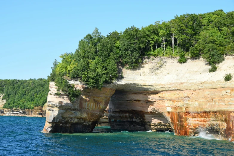 a rock formation in the middle of a body of water, michigan, giant archways, slide show, trees and cliffs