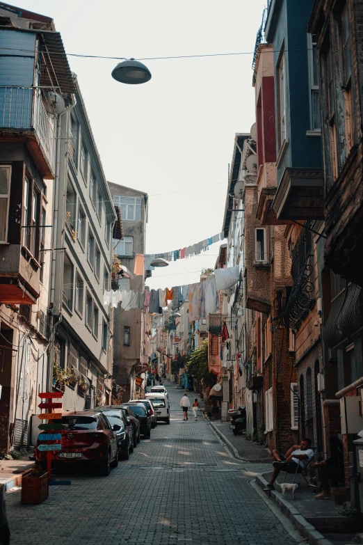 a street lined with parked cars next to tall buildings, a colorized photo, pexels contest winner, renaissance, istanbul, narrow and winding cozy streets, gif, built on a steep hill