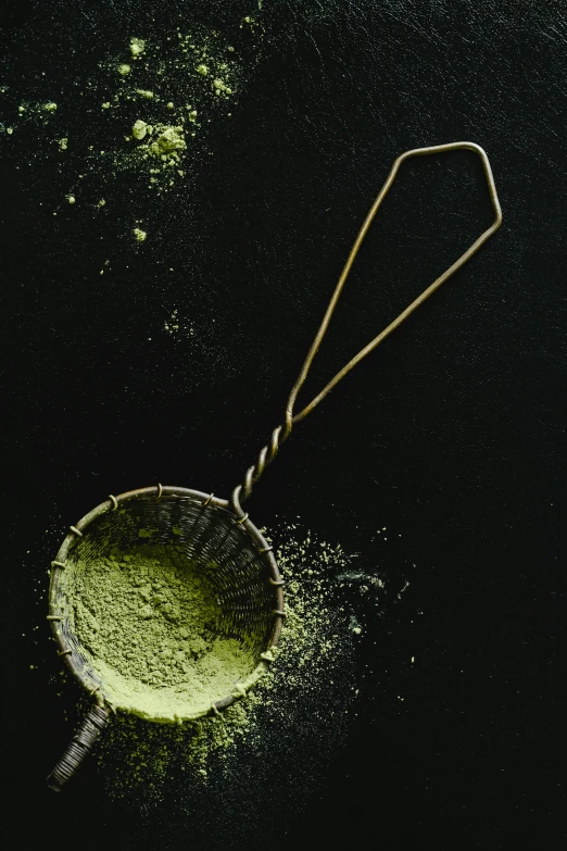 a scoop of matcha powder on a black surface, 1960s color photograph, david kassan, promo image, ornament