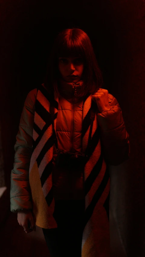 a woman standing in a dimly lit room, inspired by Elsa Bleda, unsplash, moncler jacket, left eye red stripe, low quality footage, scene from live action movie