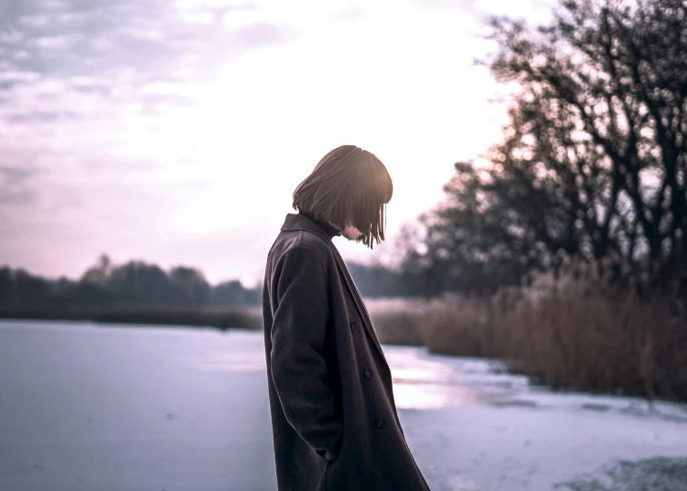 a woman standing in front of a body of water, inspired by Elsa Bleda, pexels contest winner, aestheticism, with a bob cut, wearing a long coat, sad man, teenage girl