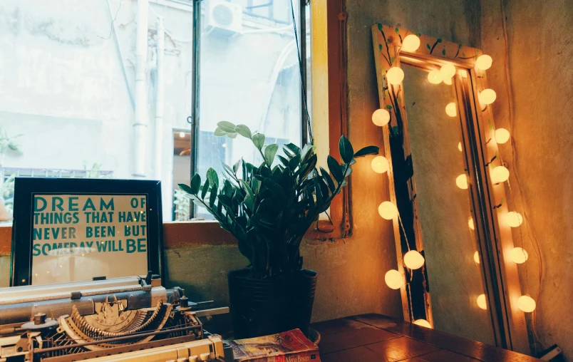 a desk topped with a typewriter next to a window, a photo, inspired by Elsa Bleda, trending on unsplash, lush plants and lanterns, standing in front of a mirror, small room in tokyo, flashing lights