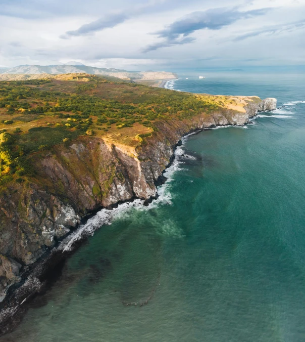 a large body of water next to a lush green hillside, by Sven Erixson, pexels contest winner, coastal cliffs, high angle uhd 8 k, conde nast traveler photo, extreme detail 8 k photo quality