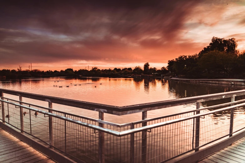 a bridge over a body of water at sunset, a picture, inspired by George Pirie, unsplash contest winner, caulfield, lake in foreground, swanland, twilight ; wide shot