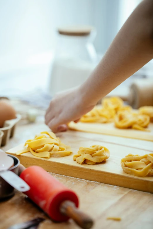 a close up of a person preparing food on a table, pasta, on a wooden tray, swirls, different sizes