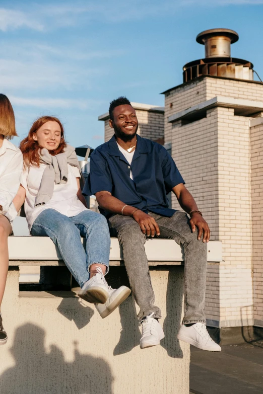 a group of people sitting on top of a building, smiling, looking away from the camera, portrait featured on unsplash, blue jeans and grey sneakers