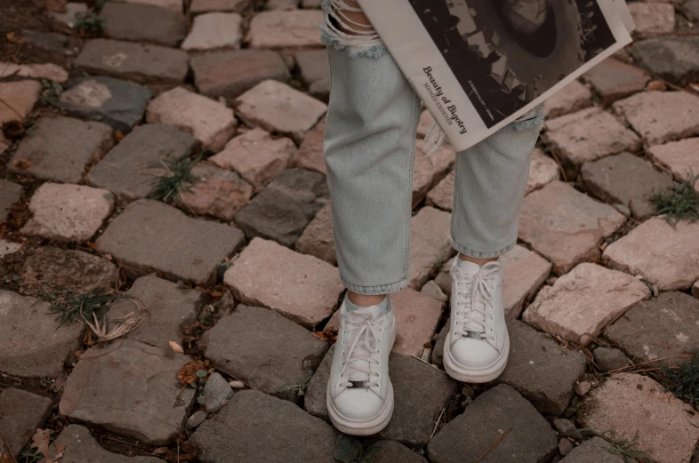 a person holding a newspaper on a cobblestone street, pexels contest winner, wearing off - white style, jean pants, 15081959 21121991 01012000 4k, white shoes
