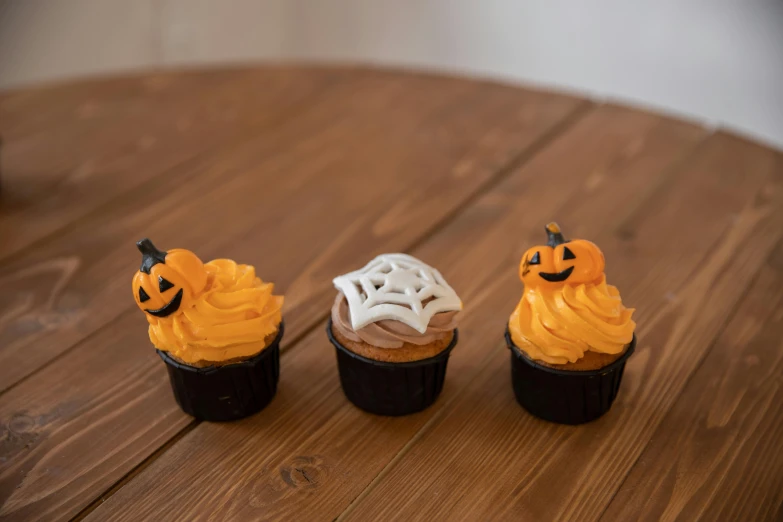 three cupcakes sitting on top of a wooden table, jack - o'- lantern, various sizes, full product shot, 3 - piece