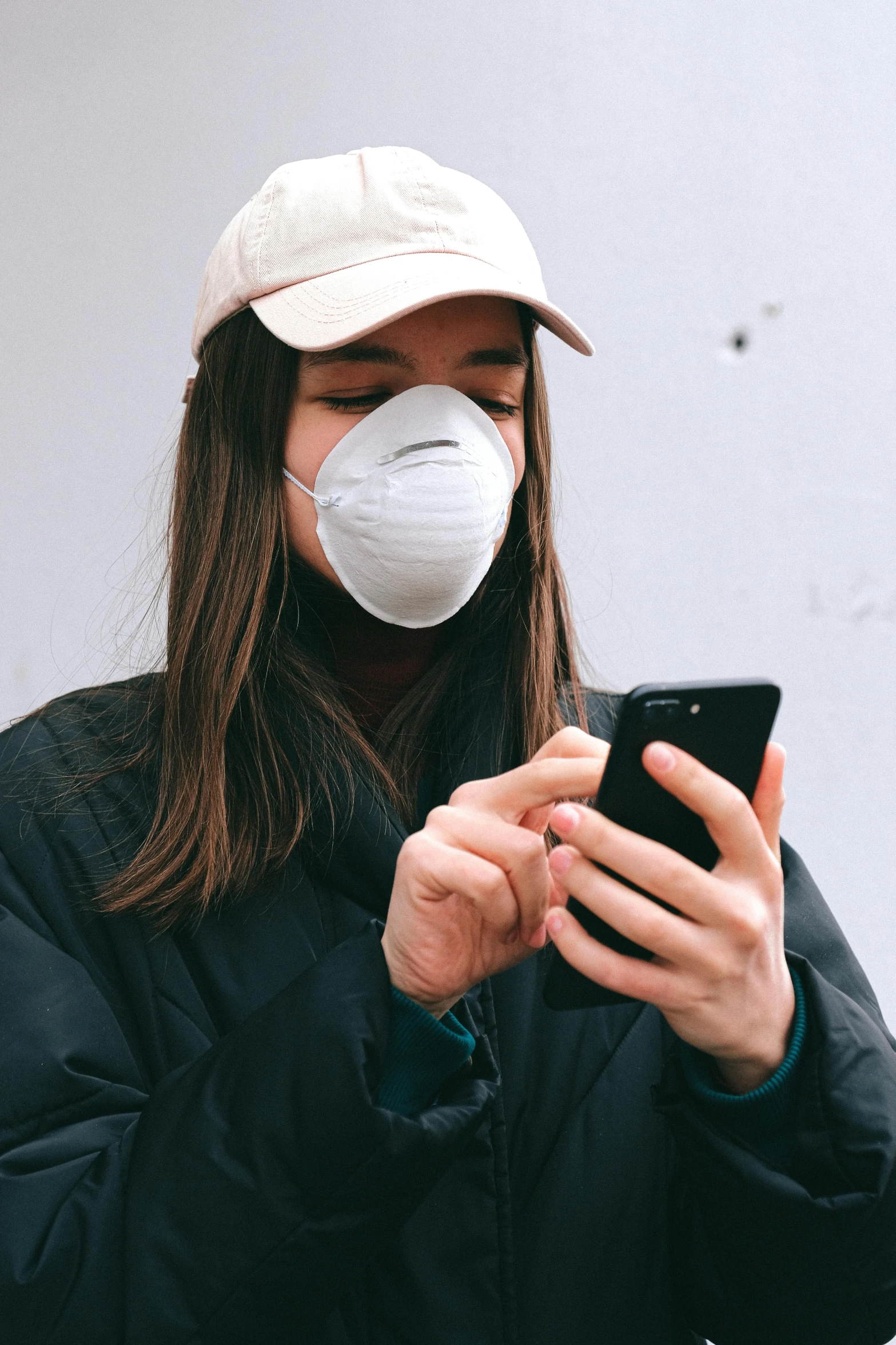 a woman wearing a face mask looking at her phone, trending on pexels, on a gray background, trending on r/streetwear, scientific, taken in the late 2010s