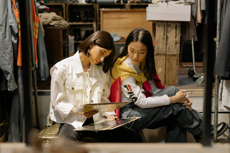 a couple of women sitting next to each other, a picture, trending on unsplash, visual art, working clothes, wearing off - white style, in a workshop, magazine photo