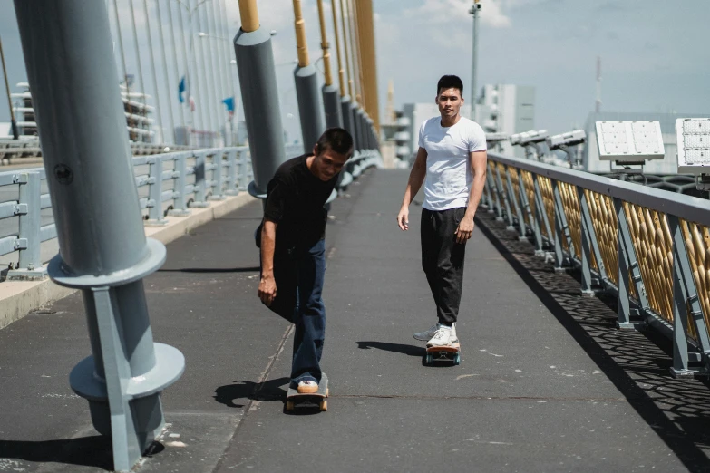 a couple of men riding skateboards across a bridge, a picture, happening, background image, thumbnail, petros and leonid, confident stance