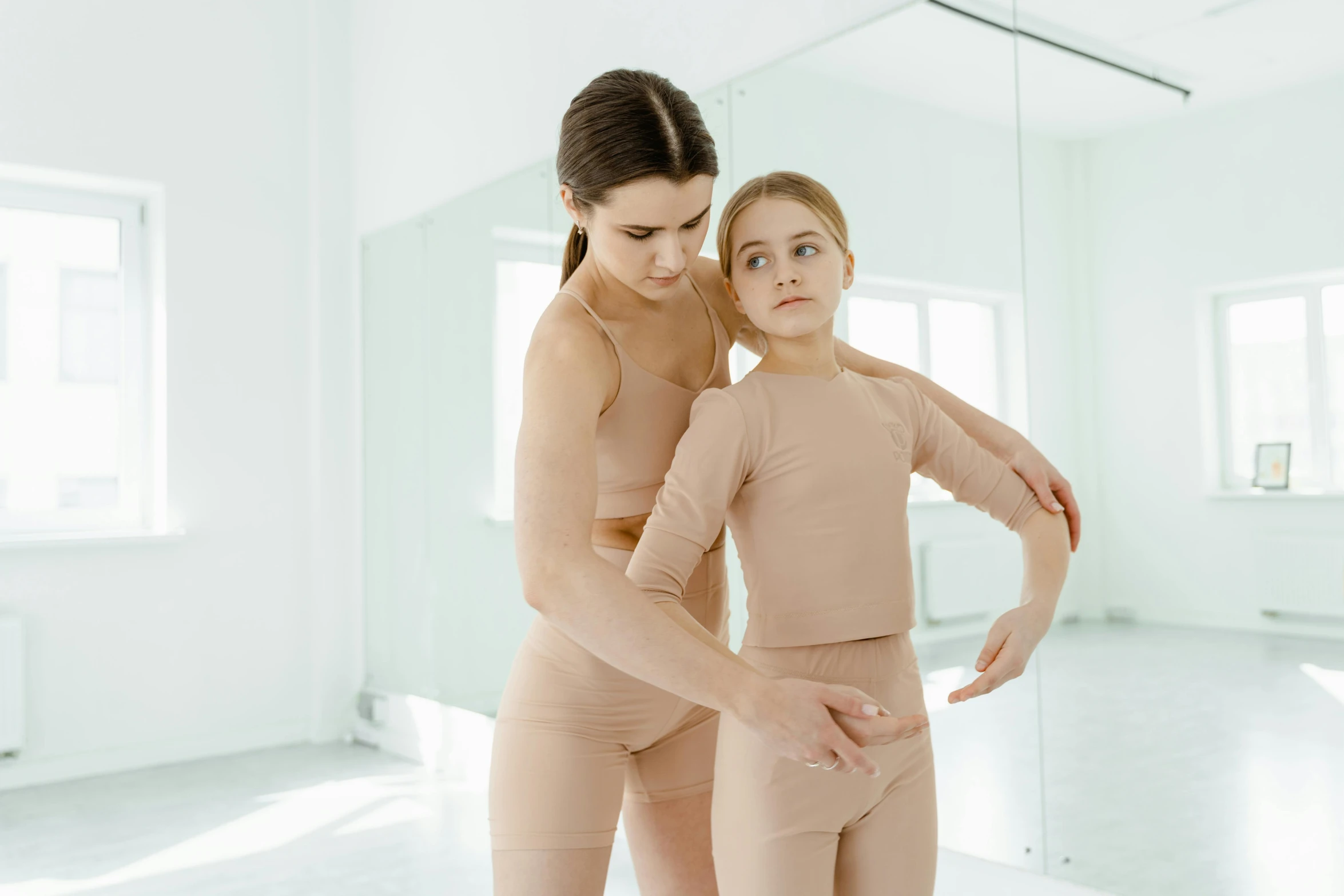 a woman standing next to another woman in a dance studio, a picture, trending on pexels, child, wearing tight simple clothes, nikolay georgiev, brown