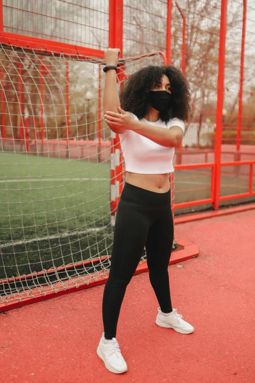 a woman holding a tennis racquet on a tennis court, by Adam Marczyński, masked, dynamic stretching, wearing a crop top, on a football field