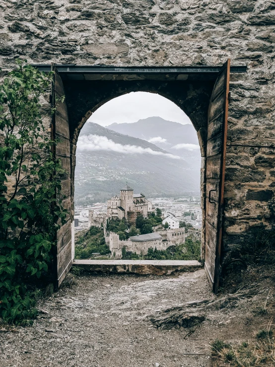 an open door with a view of a town in the distance, by Johannes Voss, unsplash contest winner, epic castle, alpes, archways made of lush greenery, grey