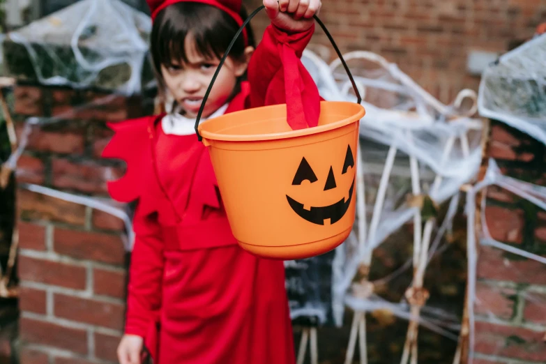 a little girl in a halloween costume holding a bucket, pexels, light red and deep orange mood, detail shot, wearing headmistress uniform, instagram post