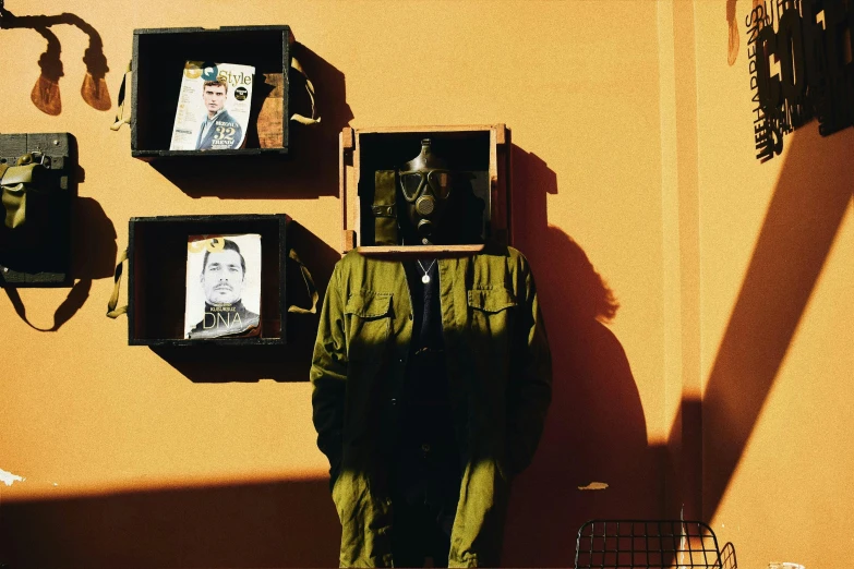 a person standing in front of a wall with pictures on it, an album cover, by Pablo Rey, unsplash, visual art, soldier with a gasmask, storefront, in the sun, cardboard cutout