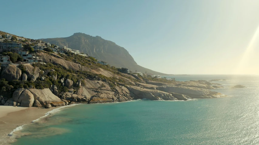 a large body of water sitting on top of a sandy beach, a matte painting, by Lee Loughridge, pexels contest winner, south african coast, wes anderson film screenshot, wide aerial shot, mountains and ocean