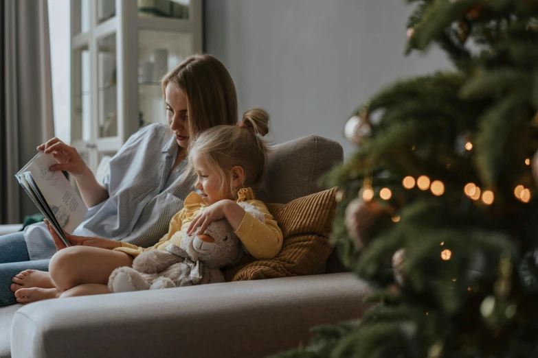 a woman and child sitting on a couch in front of a christmas tree, pexels contest winner, reading a book, everything fits on the screen, profile image, girls resting