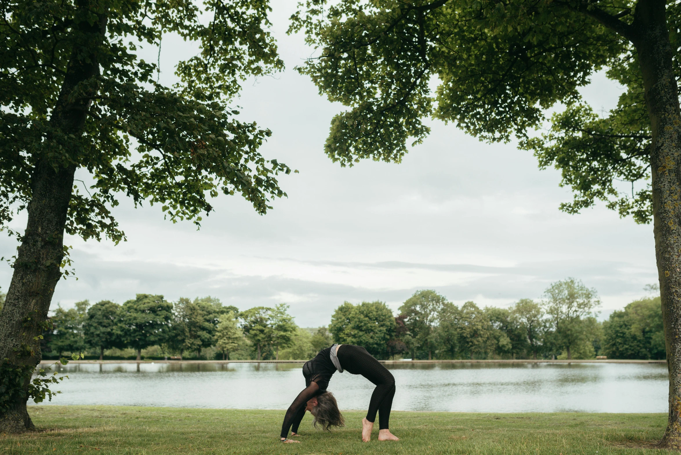 a man doing a handstand in front of a lake, by Rachel Reckitt, land art, an archway, stretching her legs on the grass, owen gent, near a lake
