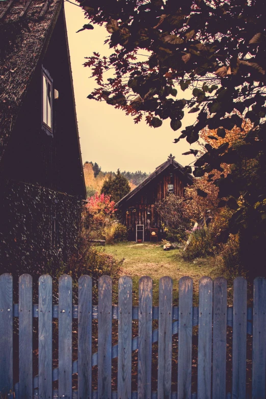 a close up of a fence with a house in the background, by Sebastian Spreng, pexels contest winner, vintage color photo, witch cottage in the forest, small scandinavian!!! houses, fall season