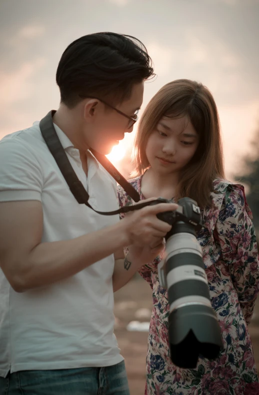 a man standing next to a woman holding a camera, darren quach, soft sunset lighting, asian girl, high-quality photo