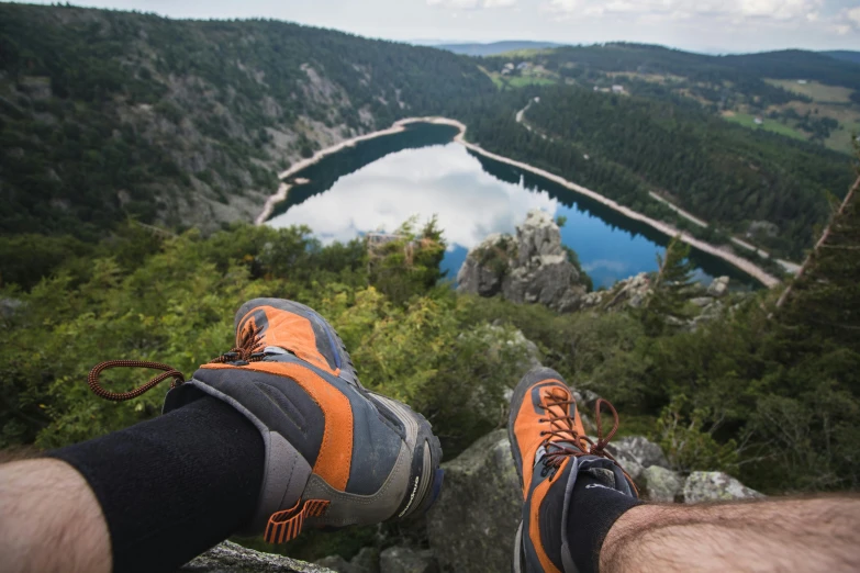 a man sitting on top of a rock next to a lake, by Jakob Gauermann, pexels contest winner, renaissance, human back legs and sneakers, grey orange, high above treeline, huge chasm