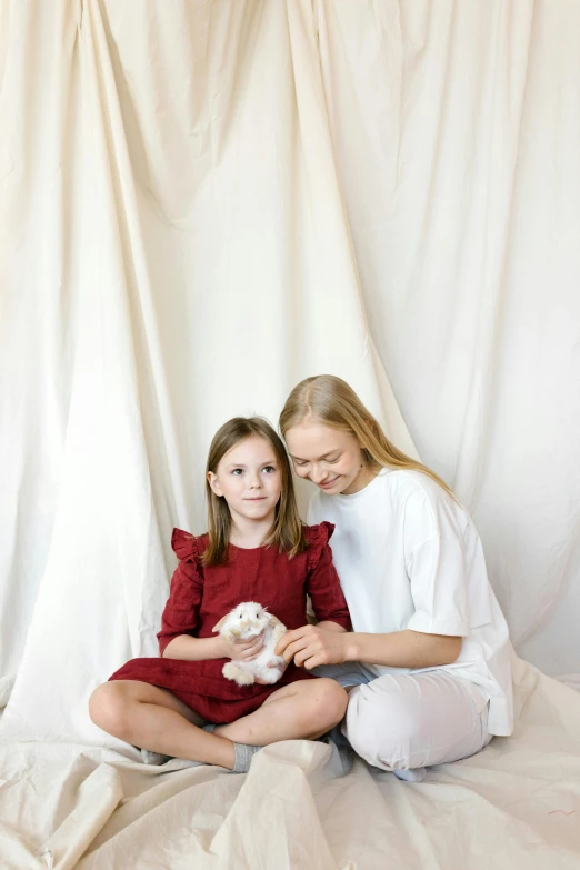 a woman and a little girl sitting on a bed, unsplash, fine art, holding a white fluffy kitten, in front of white back drop, red velvet, greta thunberg