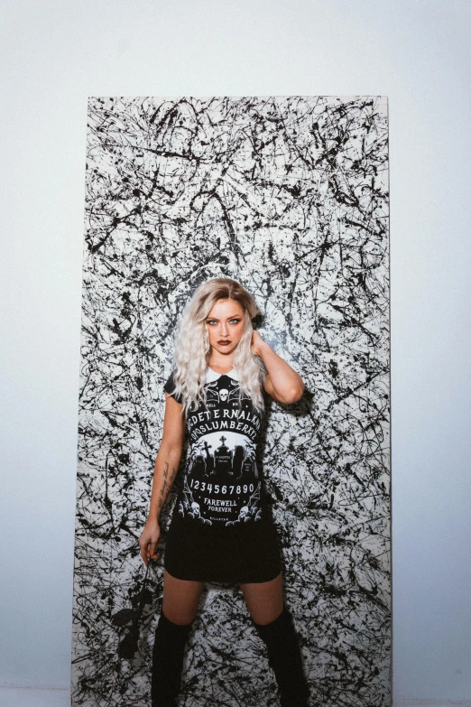a woman standing in front of a black and white wall, inspired by Elsa Bleda, graffiti, killstar, blonde girl in a cosmic dress, official store photo, on a gray background