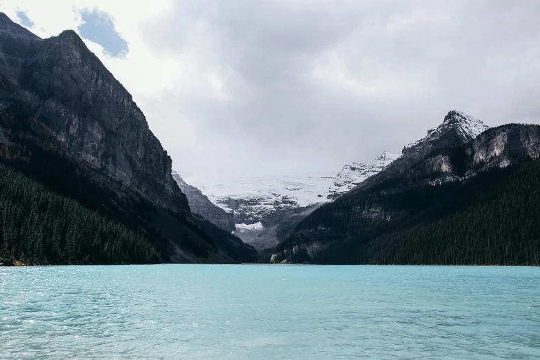 a body of water with mountains in the background, pexels contest winner, banff national park, blue glacier, low quality footage, overcast skies