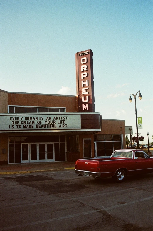 a red car is parked in front of a theater, a photo, by Pamela Ascherson, oklahoma, trending on artforum, 2000s photo, billboard image