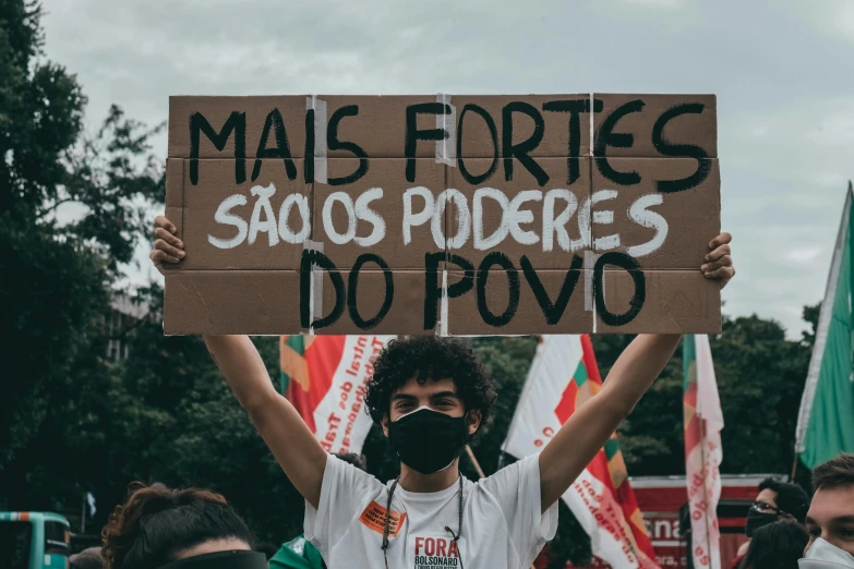 a man holding a sign in front of a crowd, by Olivia Peguero, pexels, antipodeans, amazon indian peoples in brazil, fortresses, green and red tones, fortninte