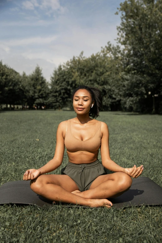a woman sitting on a yoga mat in a park, an album cover, trending on pexels, black woman, lotus pose, calm face, bralette
