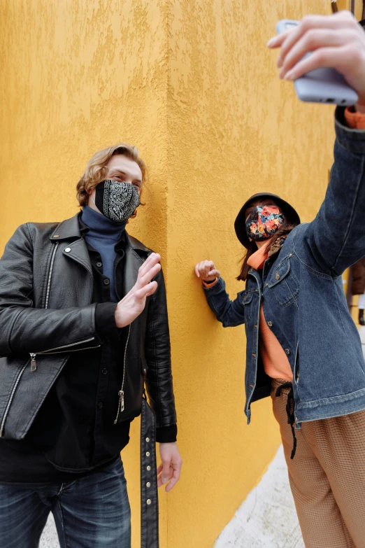 two men standing next to each other in front of a yellow wall, a picture, trending on pexels, graffiti, black bandana mask, wearing a turtleneck and jacket, taking a picture, felix englund