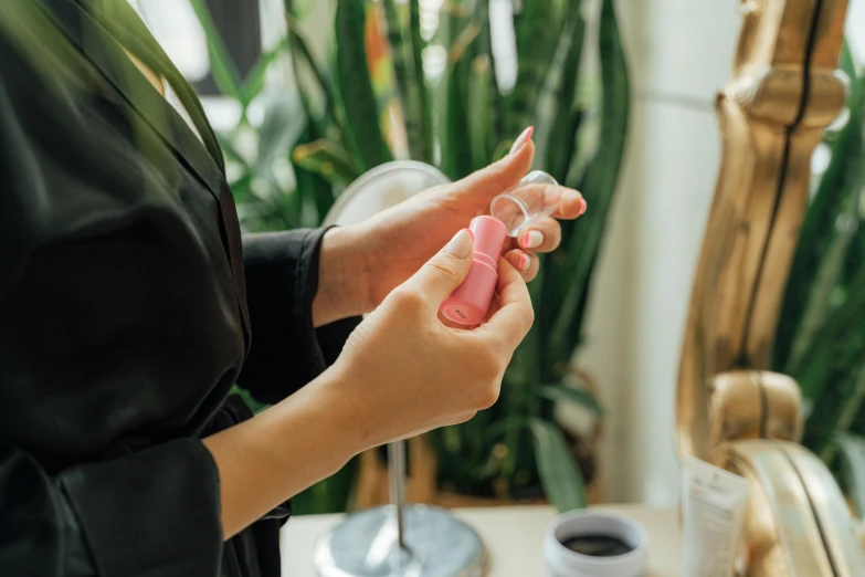 a close up of a person holding a pink object, by Emma Andijewska, trending on pexels, happening, skincare, holding a bottle, vibrating, back of hand on the table