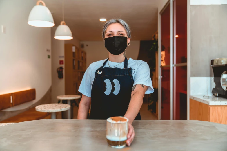 a woman wearing a face mask behind a counter, a portrait, pexels contest winner, private press, latte art, thumbnail, spanish, slightly minimal