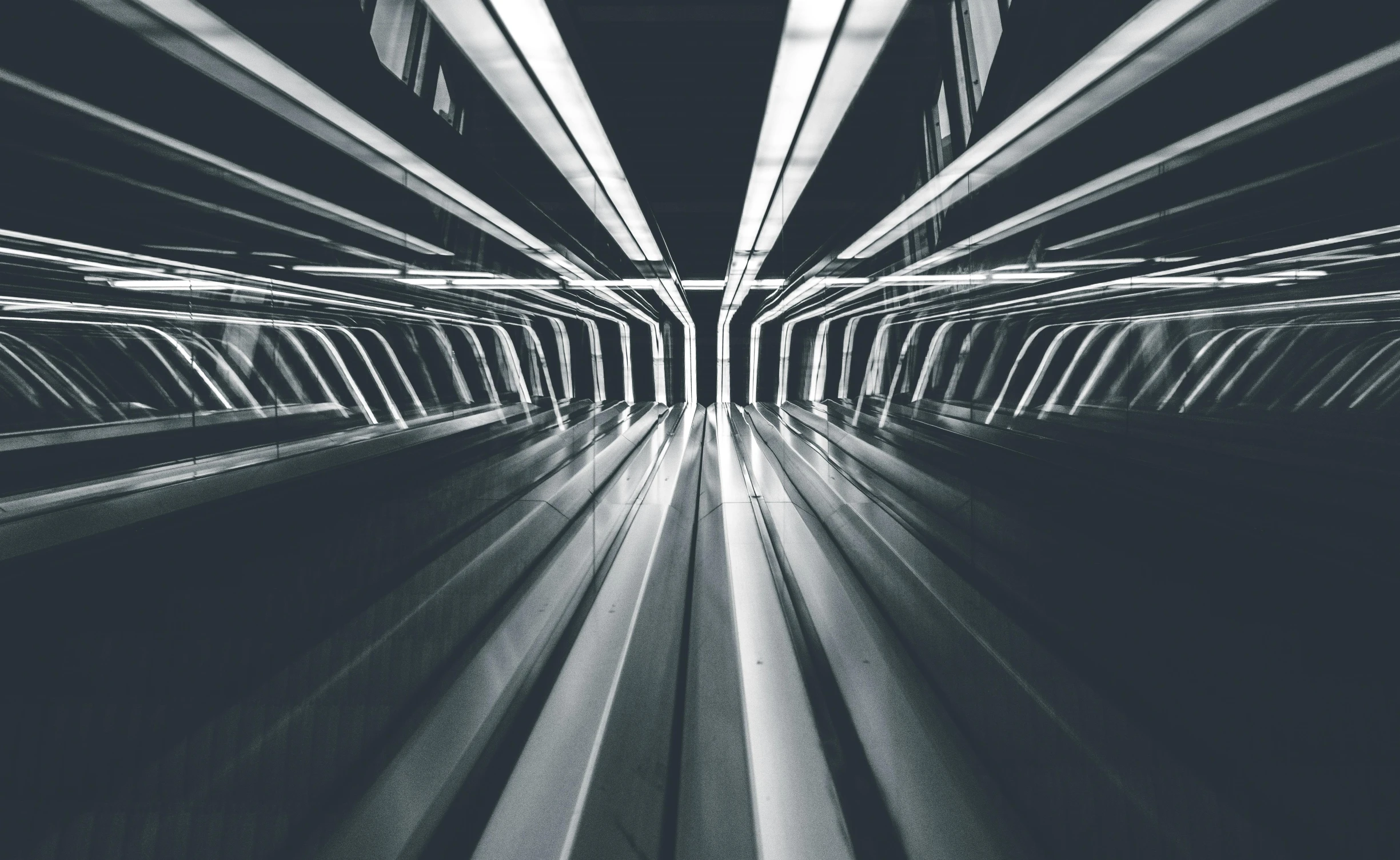 a black and white photo of an escalator, by Adam Marczyński, futurism, glowing tubes, instagram post, symmetrical background, trains