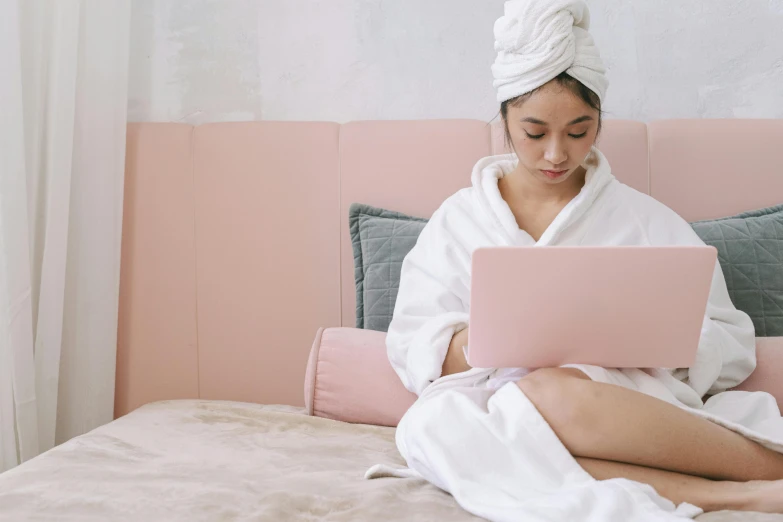 a woman sitting on a bed using a laptop, trending on pexels, happening, pastel pink robes, asian female, wearing a towel, wearing white clothes