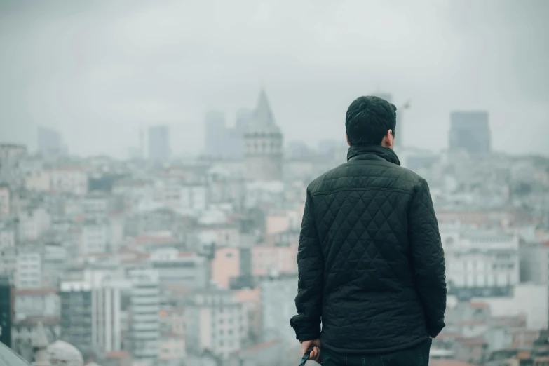 a man with a suitcase looking out over a city, pexels contest winner, happening, wearing a turtleneck and jacket, istanbul, grey sky, background image