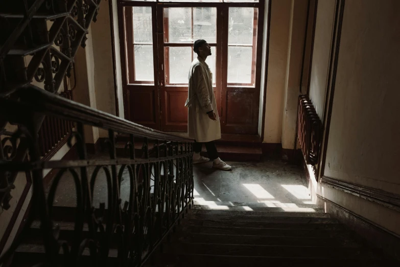 a person walking down a set of stairs, inspired by Elsa Bleda, pexels contest winner, happening, light brown trenchcoat, inside an old apartment, androgynous person, schools