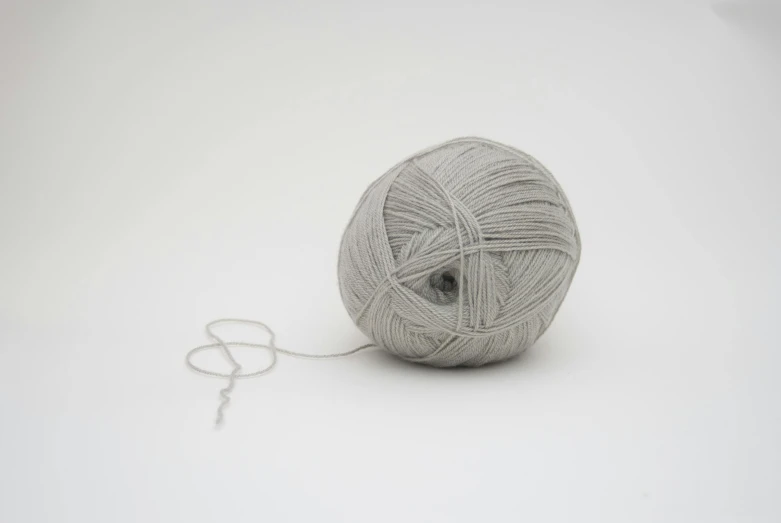 a ball of yarn on a white surface, an album cover, inspired by Cerith Wyn Evans, unsplash, arte povera, grey clothes, silver，ivory