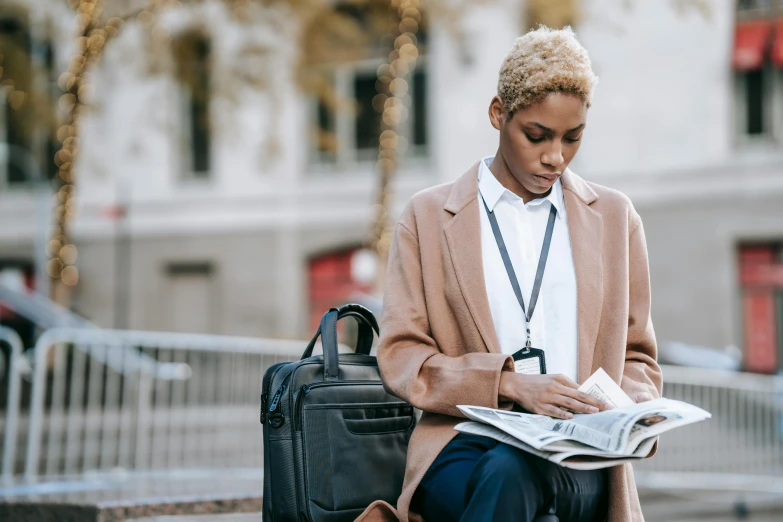 a woman sitting on a bench reading a newspaper, trending on unsplash, holding a briefcase, short blonde afro, tailored clothing, conde nast traveler photo