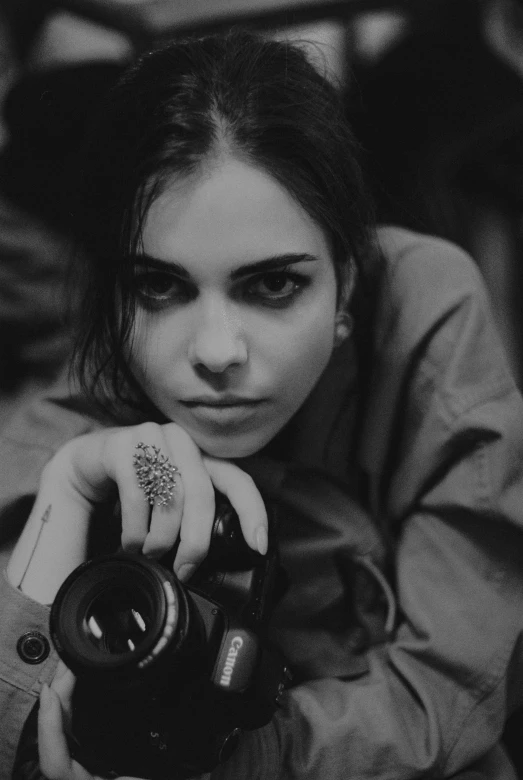 a black and white photo of a woman holding a camera, inspired by irakli nadar, cara delevingne, black hair and large eyes, grungy woman, low quality photograph