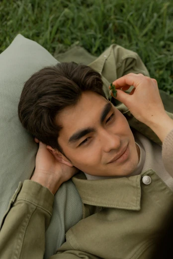 a man laying on top of a lush green field, an album cover, inspired by Zhang Han, trending on pexels, large bushy eyebrows, wearing military outfit, happy cozy feelings, laying in bed