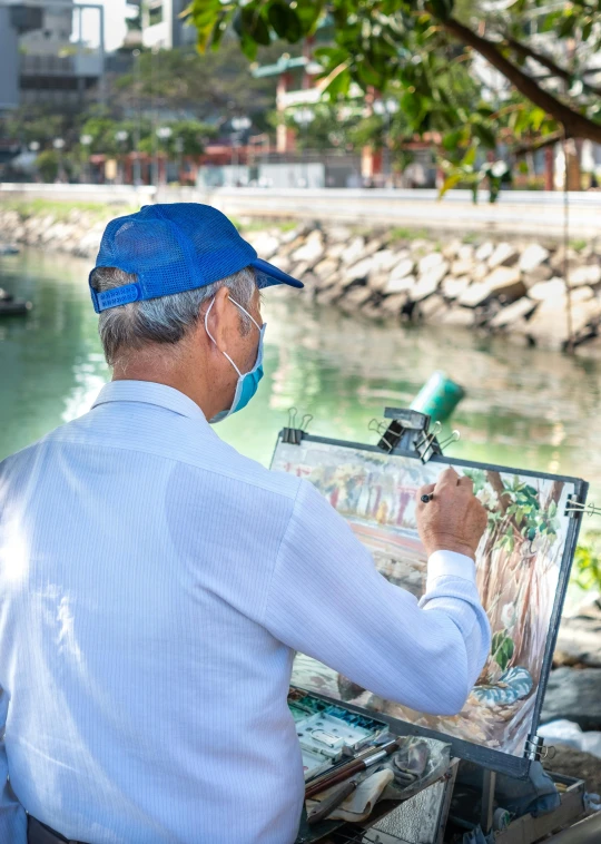 a man in a blue hat is painting, a photorealistic painting, inspired by Francesco Guardi, pexels contest winner, ao dai, at the waterside, wearing facemask and sunglasses, singapore