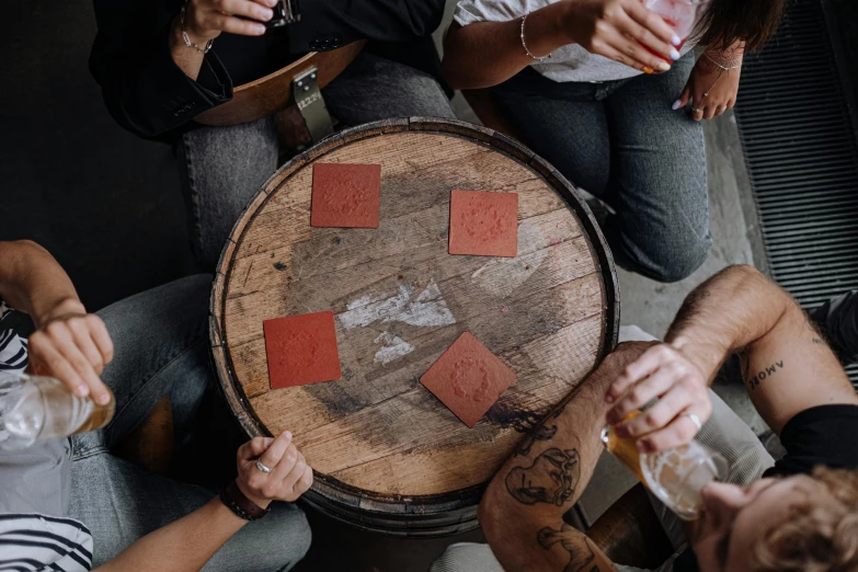 a group of people sitting around a wooden table, an album cover, pexels contest winner, card game, with a drink, leather, terracotta