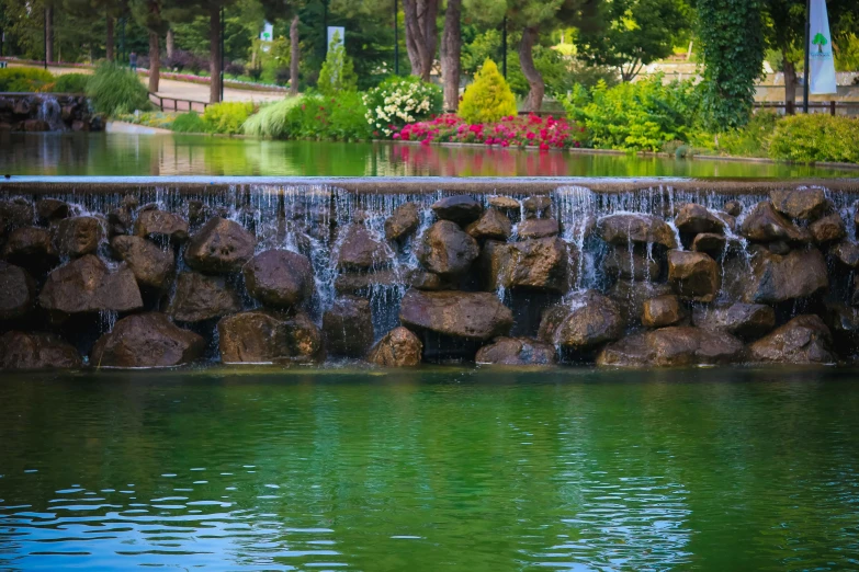 a small waterfall in the middle of a pond, by Arthur Sarkissian, unsplash, romanticism, city park with flowers, sayem reza, 2 0 2 2 photo, green waters