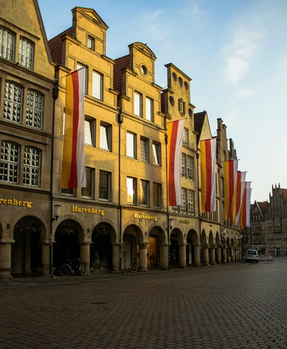 a cobblestone street lined with tall buildings, by Juergen von Huendeberg, pexels contest winner, red yellow flag, lower saxony, storefront, bargello