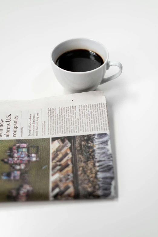 a newspaper sitting on top of a table next to a cup of coffee, a picture, high-resolution photo, up-close, image